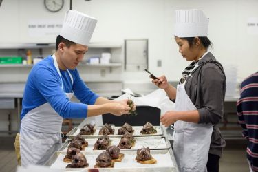 student garnishing wood pigeon while classmate takes photo