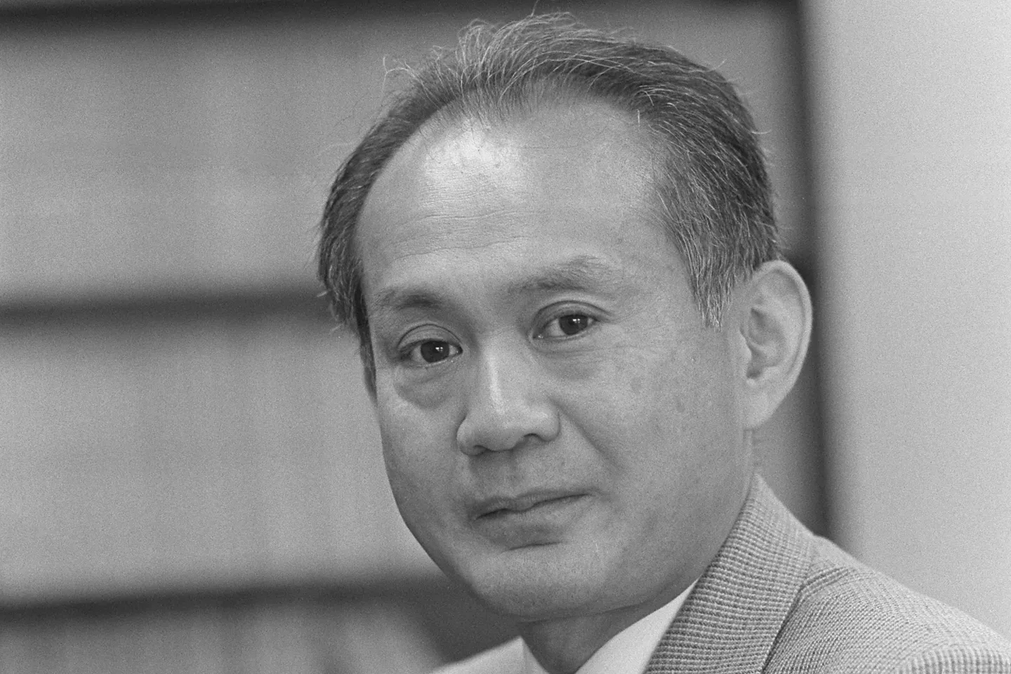 Amemiya in a light-colored suit is looking directly at the camera in a black and white portrait.