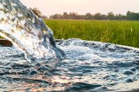 closeup of water pouring from an irrigation pipe with field in the background