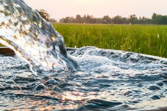 closeup of water pouring from an irrigation pipe with field in the background