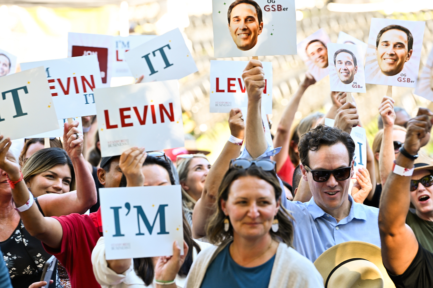 Image of audience members holding signs with President Levin's name and face.