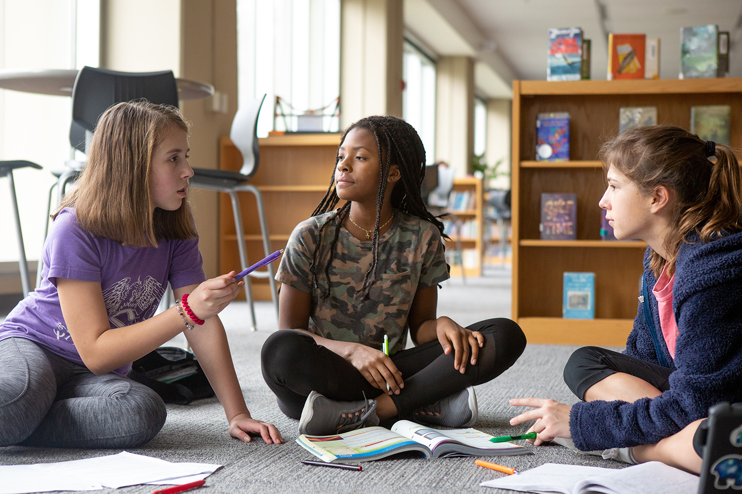 Three girls sitting on school library floor engaged in discussion