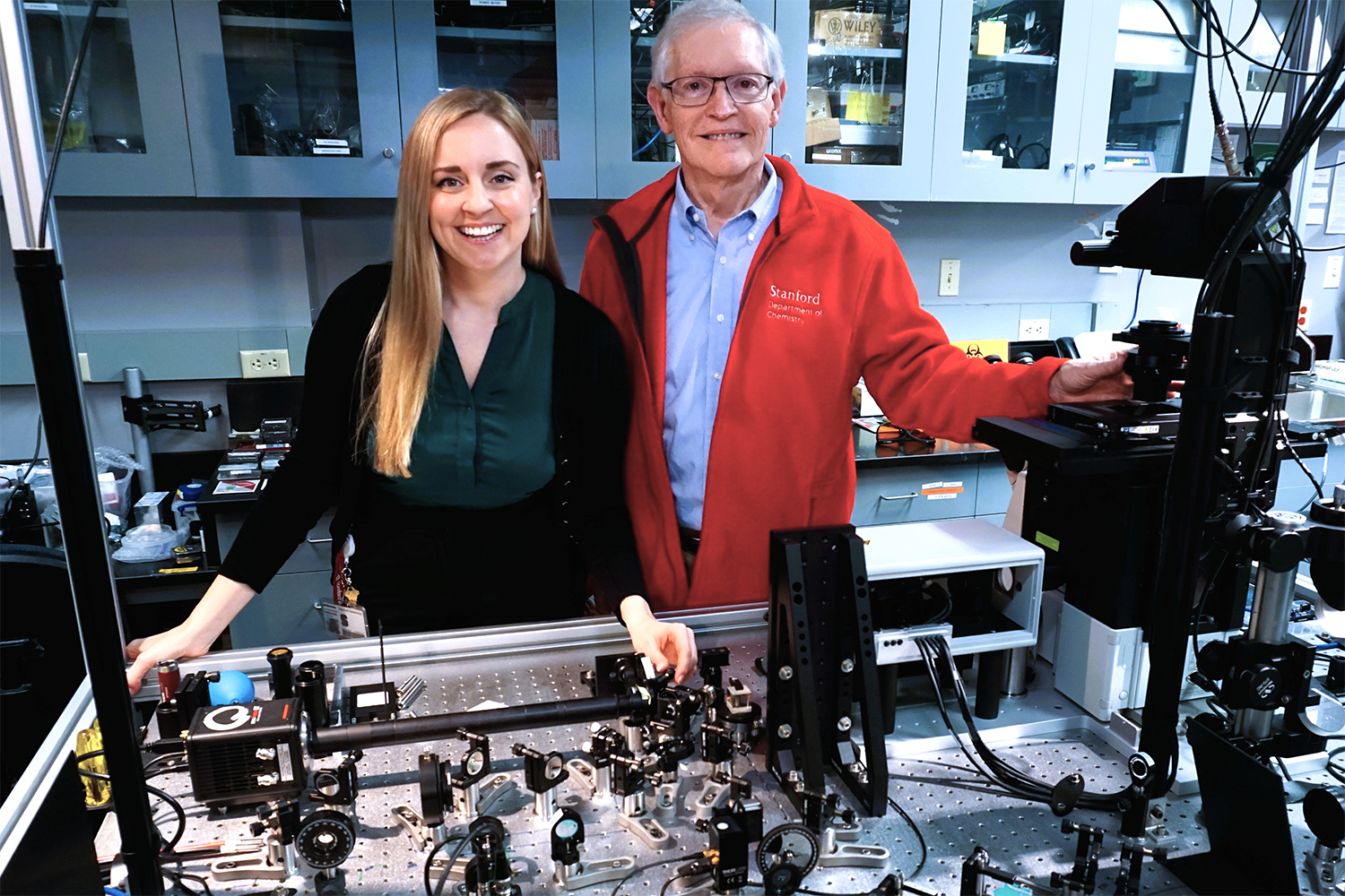 The researchers stand in a laboratory setting at a workbench filled with instruments and tools.