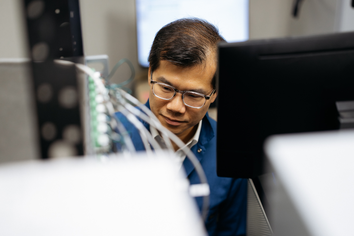 William Chueh looks closely at wired lab equipment behind a computer monitor.