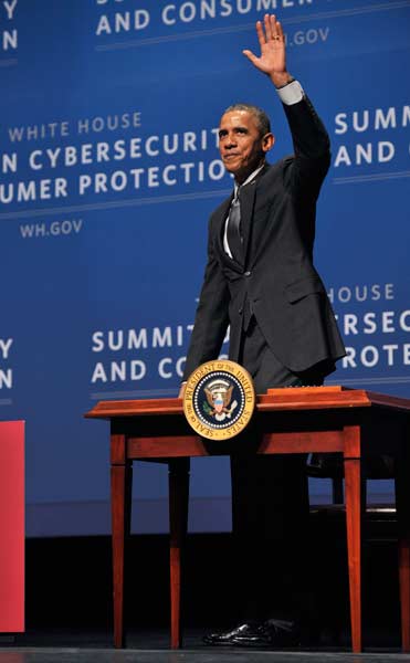 Obama standing behind a table waving to the audience.