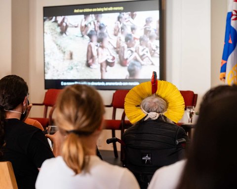 A screen showing clips from a documentary, with Chief Raoni and audience members watching