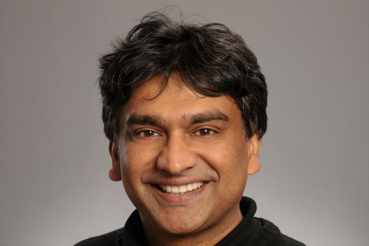 Bali Pulendran smiling into the camera against a gradient gray background.