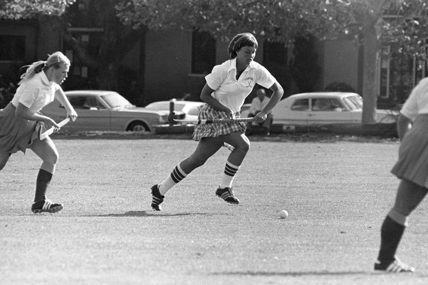 Black-and-white photo of Stanford field hockey player Onnie Killefer in a plaid skirt chasing the ball during a match.
