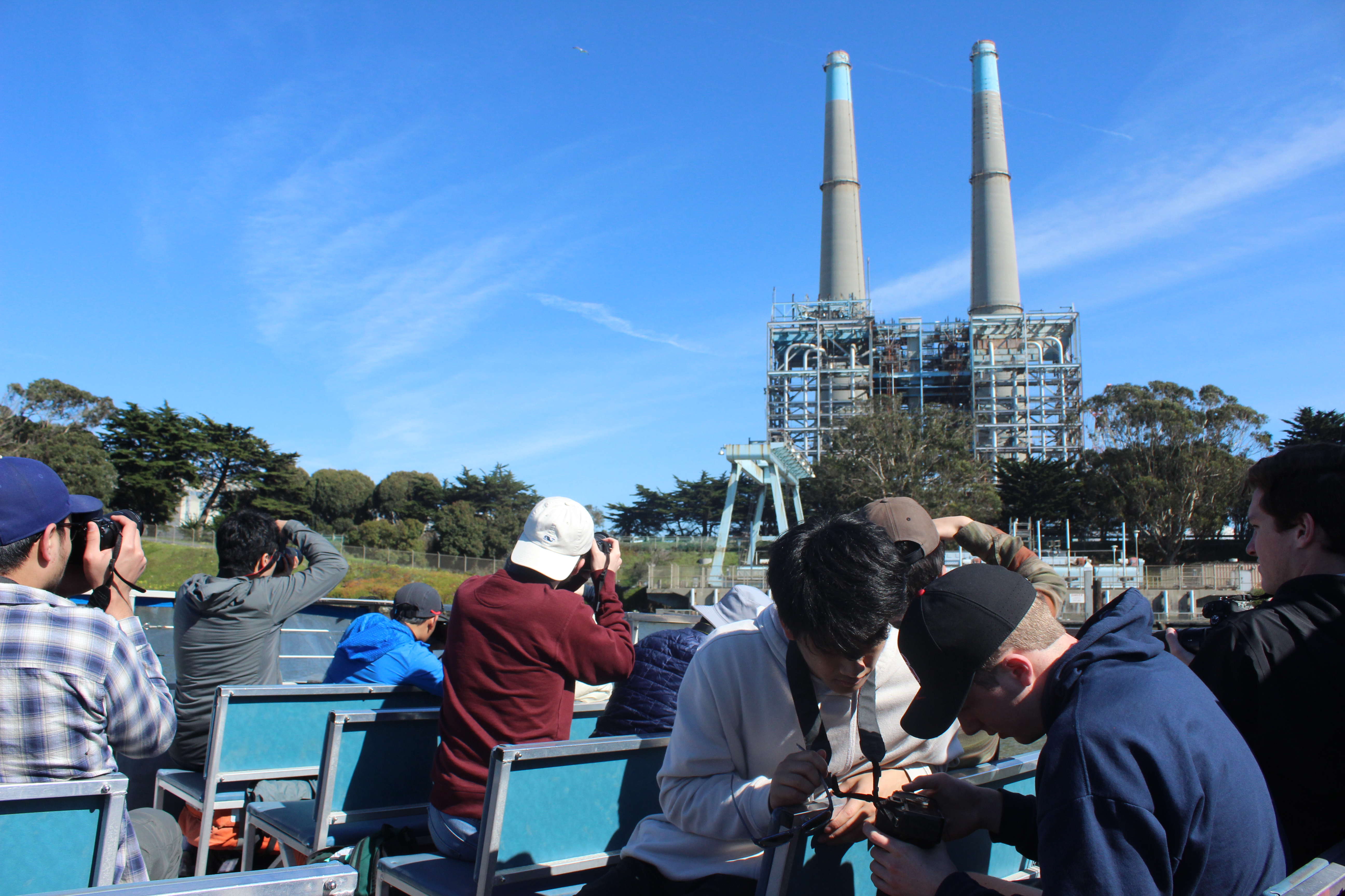 Students on a boat with cameras taking photos of a power plant