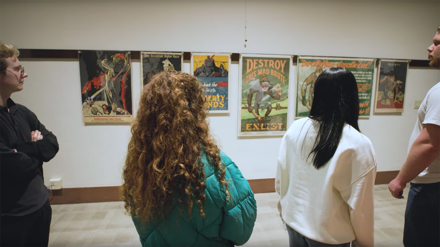 Visitors view historical propaganda posters in an exhibition space, discussing the artwork displayed on the walls.