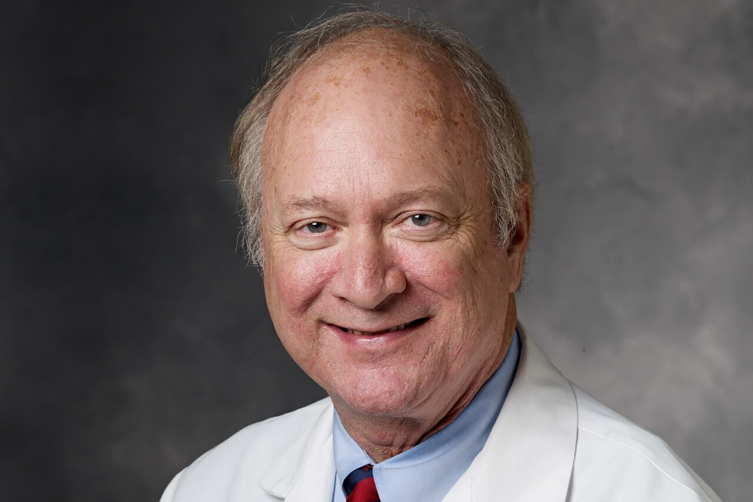 Robert Herfkens wearing a white lab coat and a blue shirt with a red tie, posed against a neutral background.