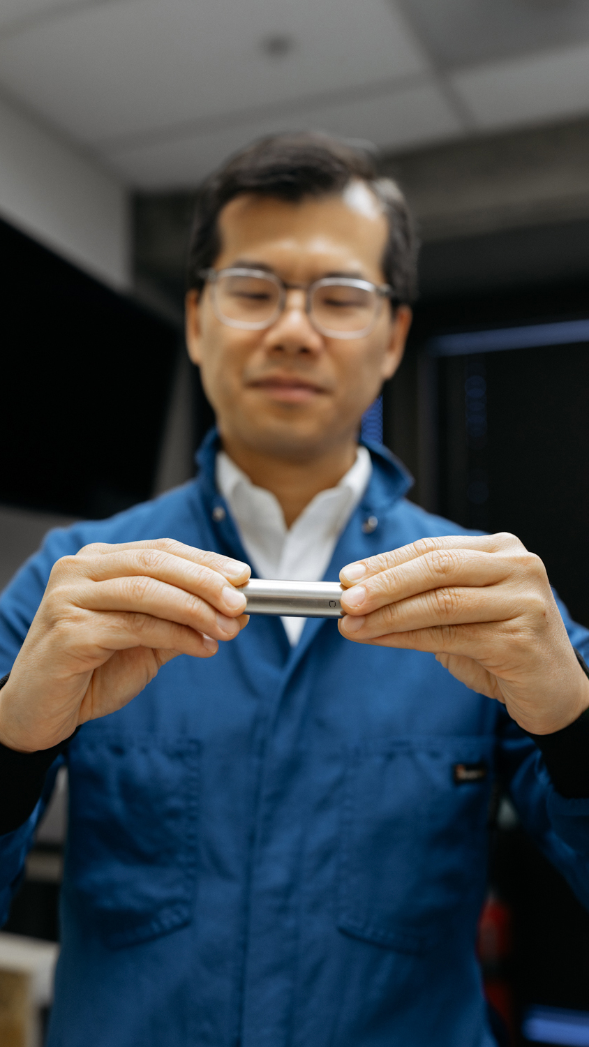 William Chueh holds a small metal cylinder in both hands, looking down at it.