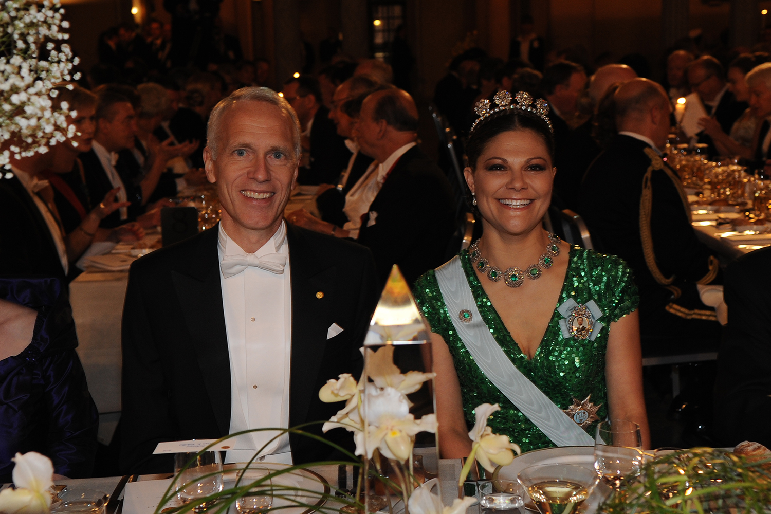 Brian Kobilka in white tie and Crown Princess Victoria of Sweden in a green sequined gown and tiara at a formal banquet.