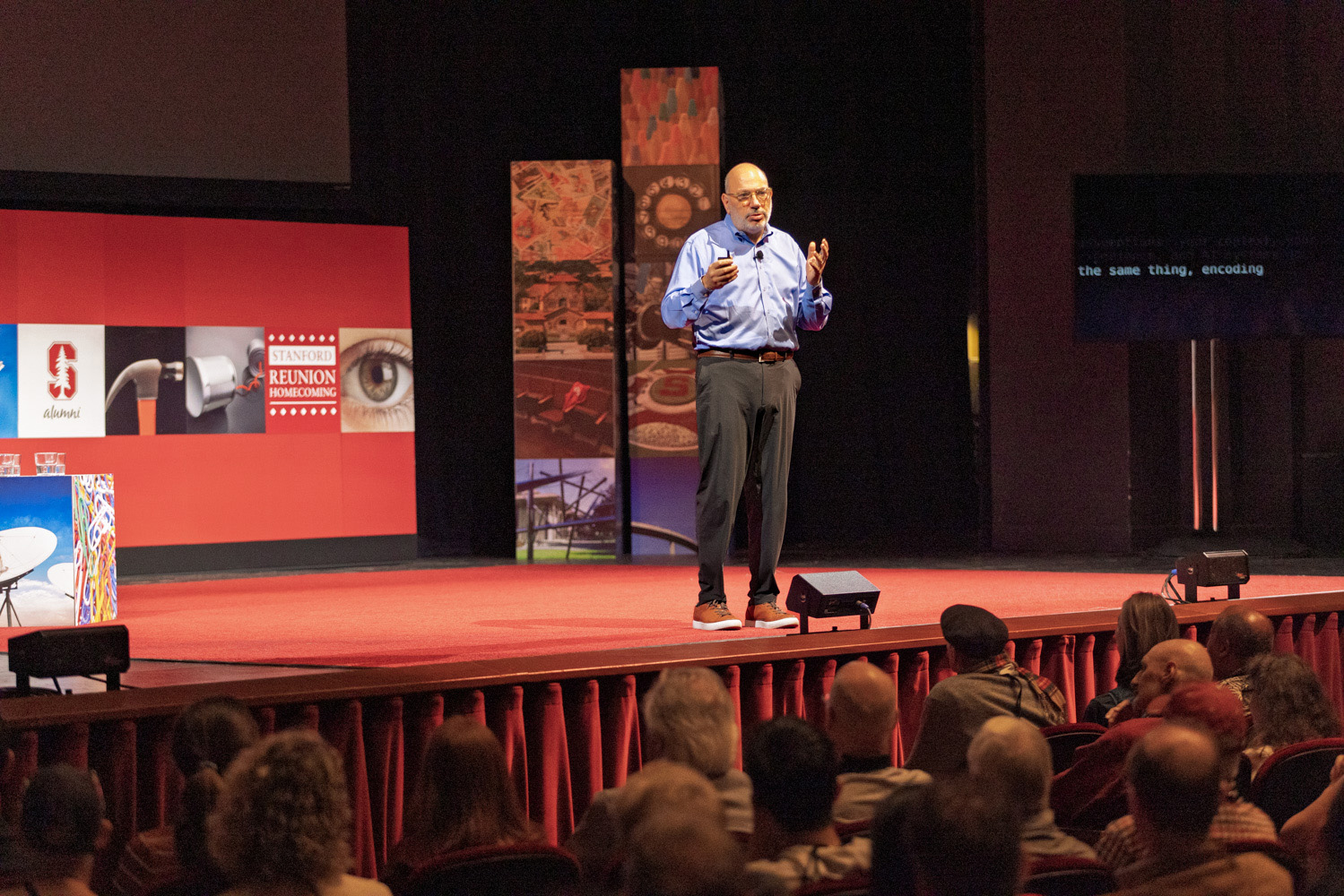 James Landay presents on a red stage to a seated audience, with event imagery on screens behind him.