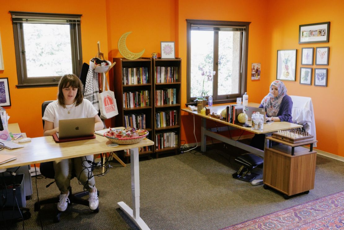 Shows the interior of the Markaz at Stanford, with two staff members seated at desks and decor including a warm orange wall.