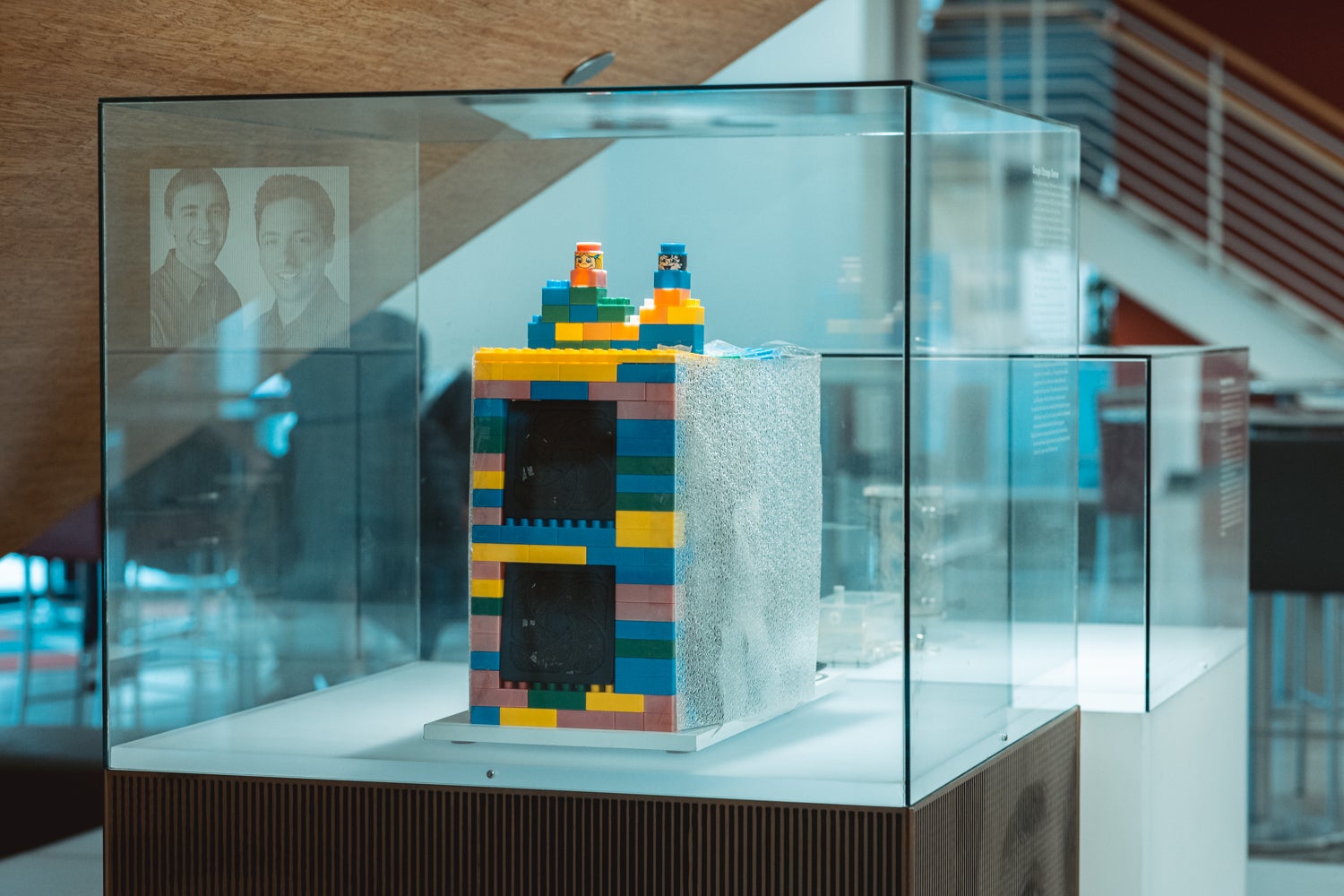 A server encased in colorful toy bricks inside a display case. An image of Sergey Brin and Larry Page can be seen in the background.