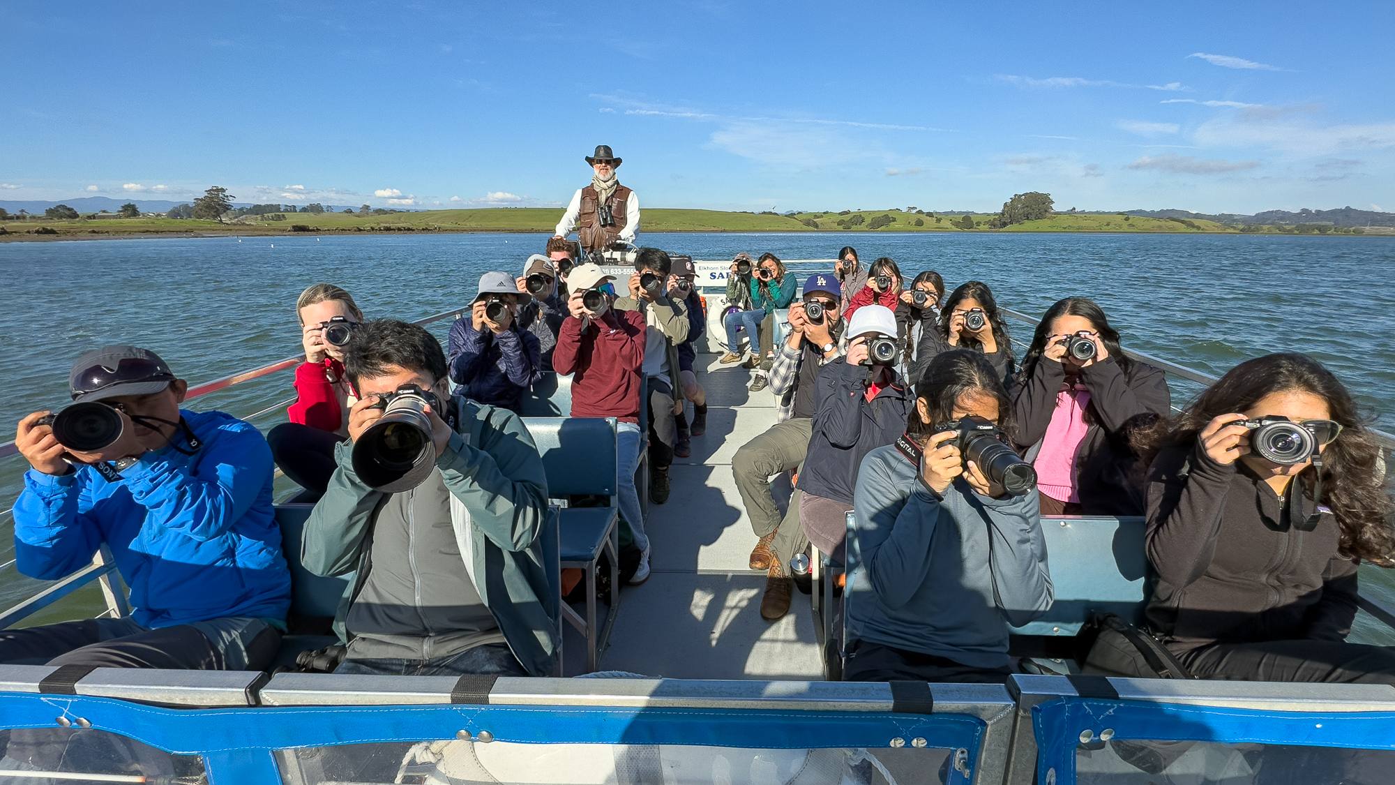 View of the tour boat, showing the captain and all of the students, seated and aiming their cameras at the photographer