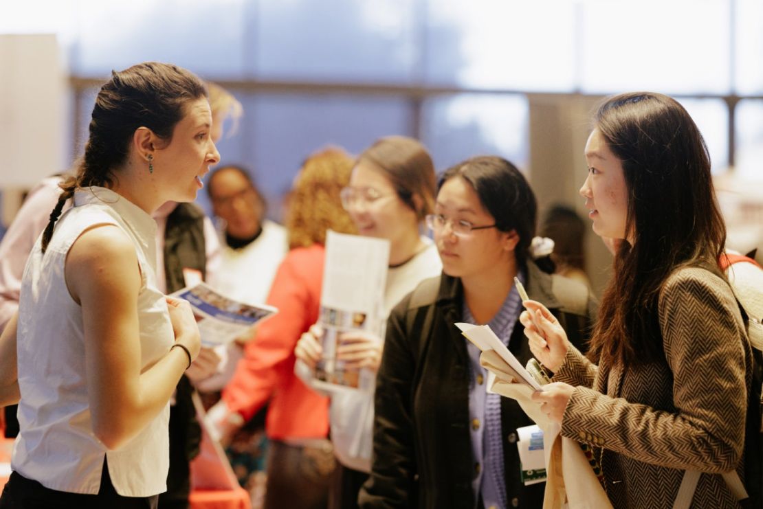 Two students talking to a potential employer inside a crowded room.
