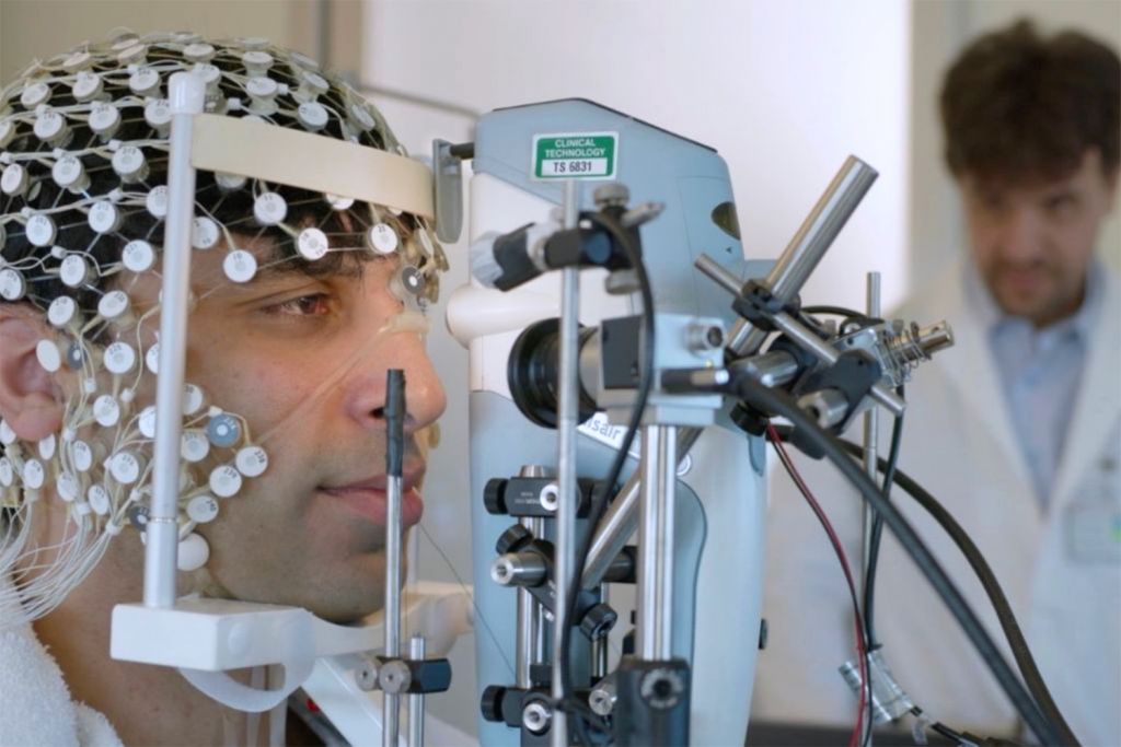 Image of Karl Deisseroth overlooking a demonstration of the “air puff test” on a person's eye.