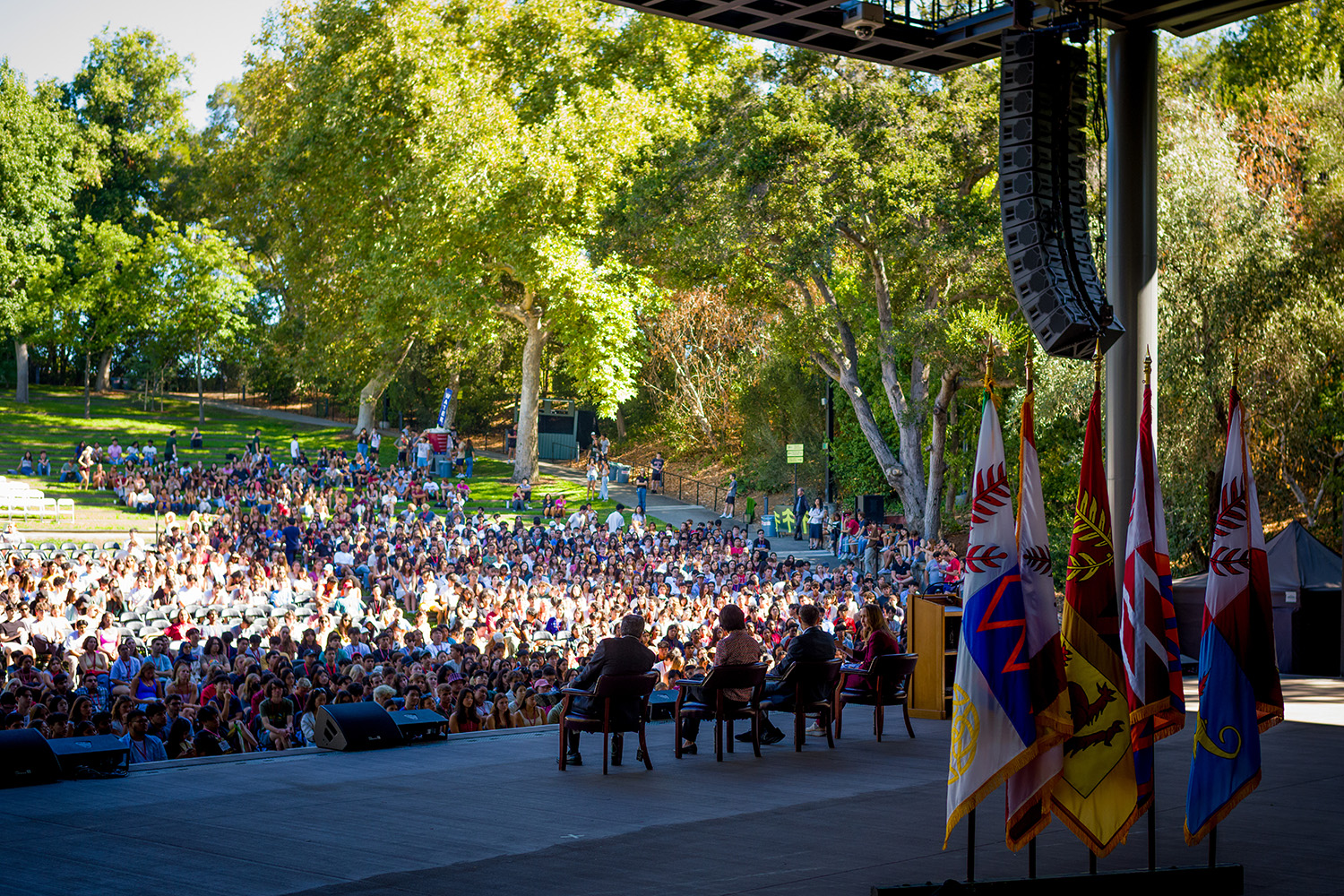 Wide shot from back of Frost Amphitheater stage silhouettes the panelists and show the student audience in attendance.