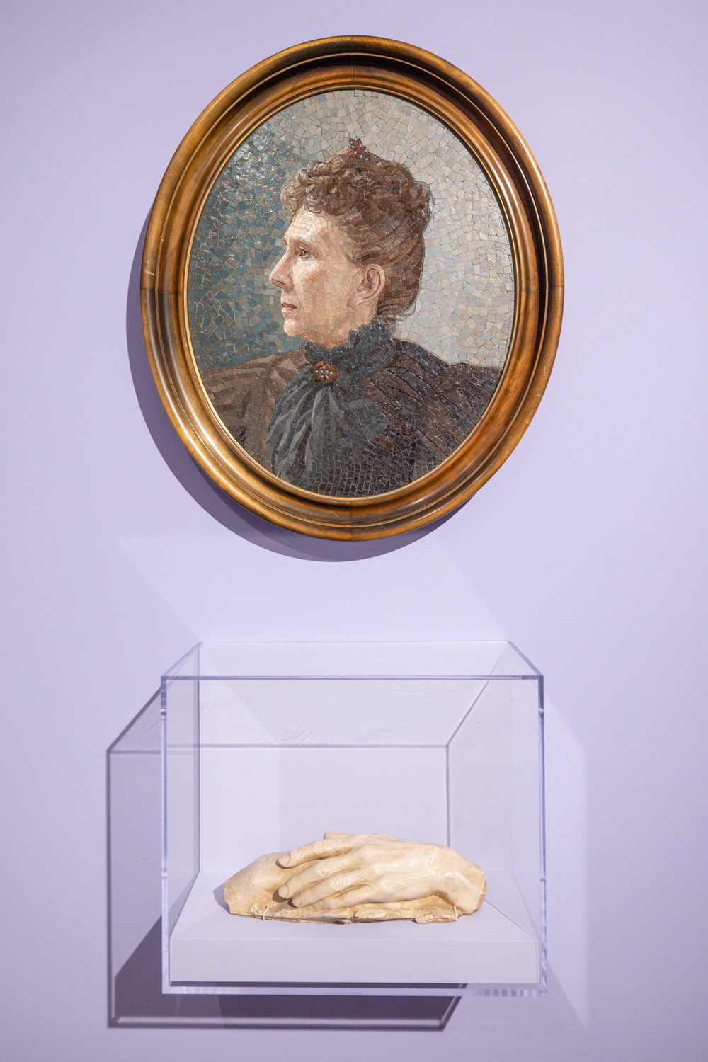 A mosaic portrait of Bertha Berner hangs above a display case containing a cast of hands of David Starr Jordan, showcased in a museum setting.
