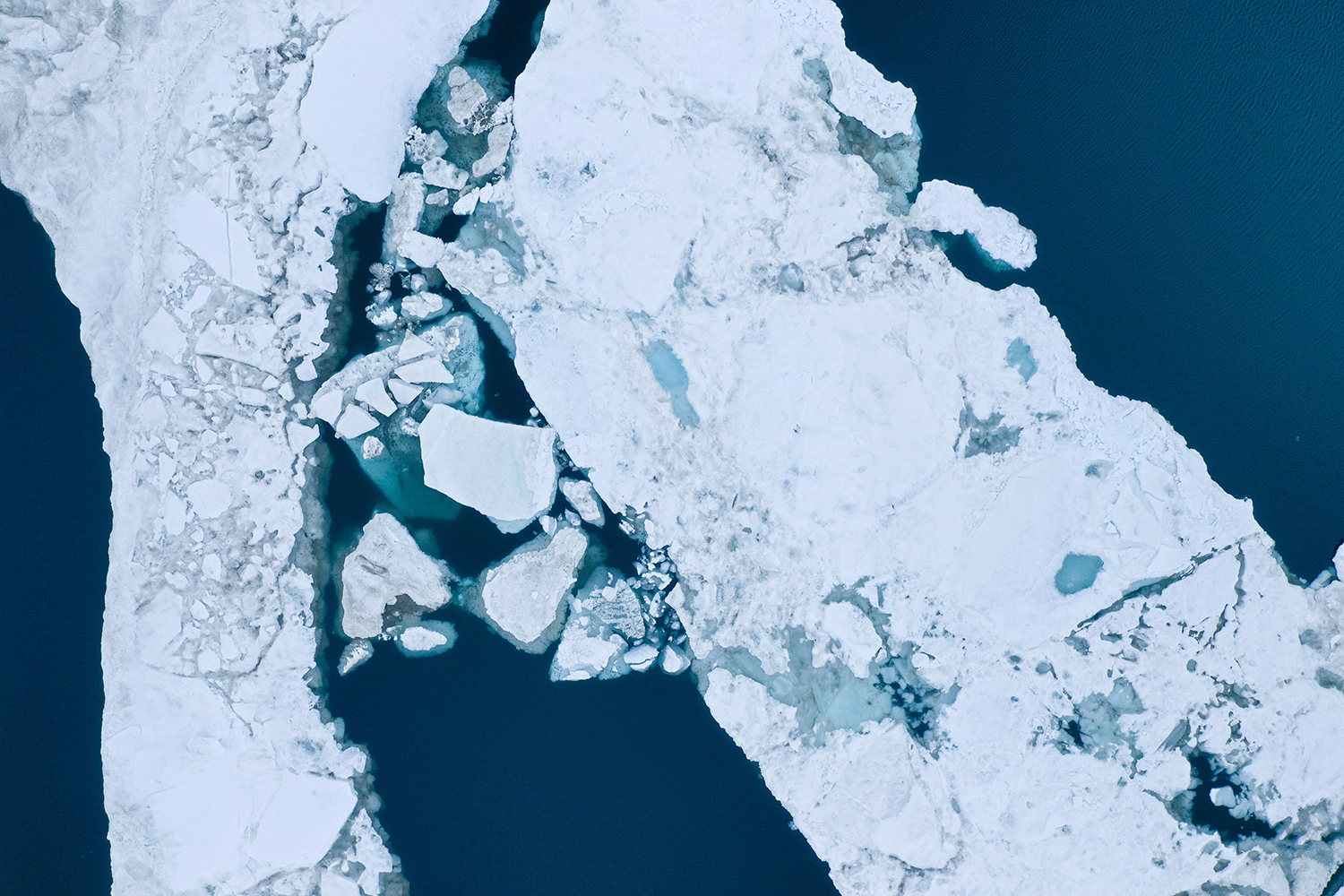 Aerial view captures fractured sea ice floes separated by channels of dark blue water.