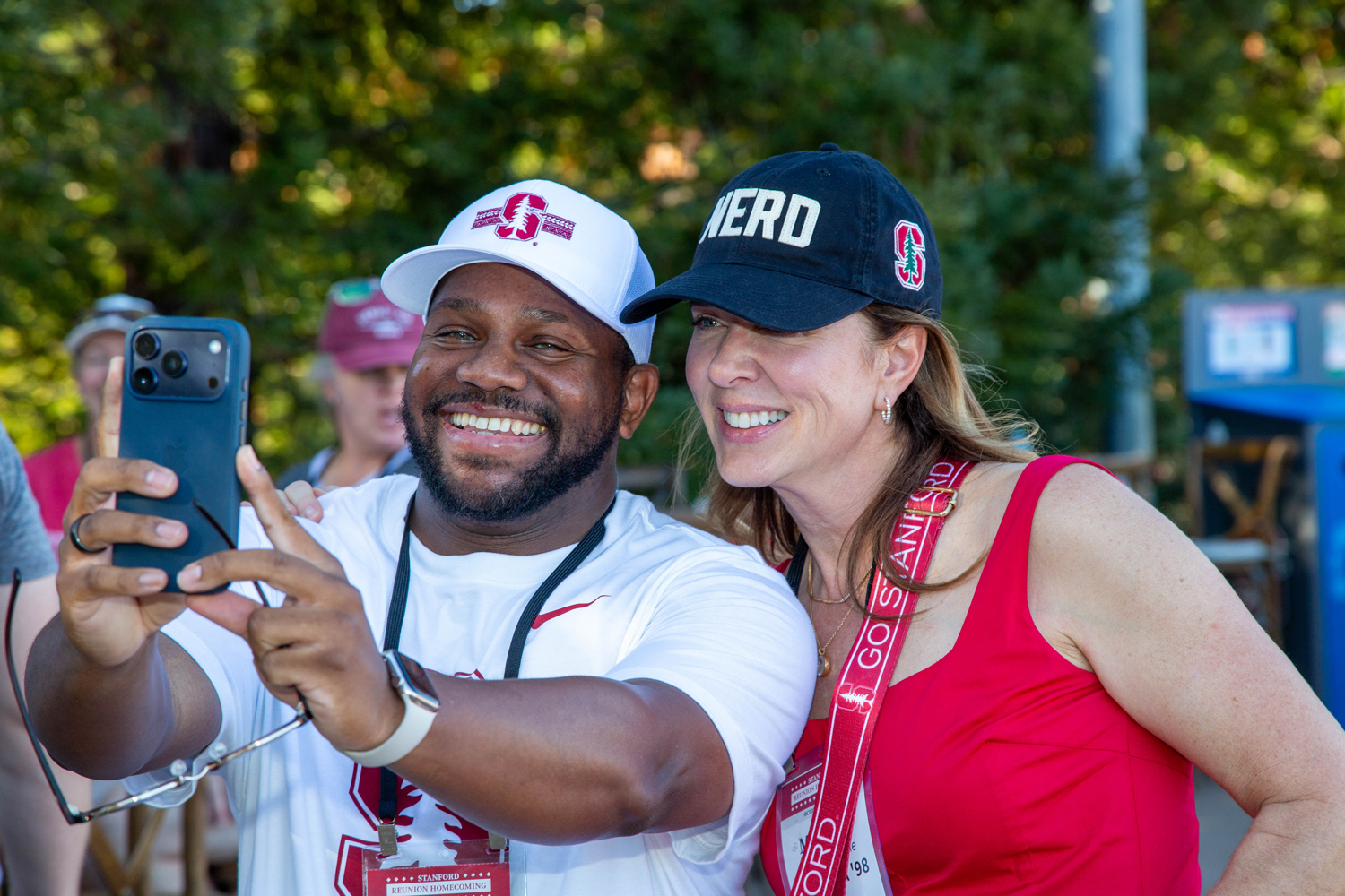 Two people in Stanford caps smile for a selfie outdoors, one holding the phone.