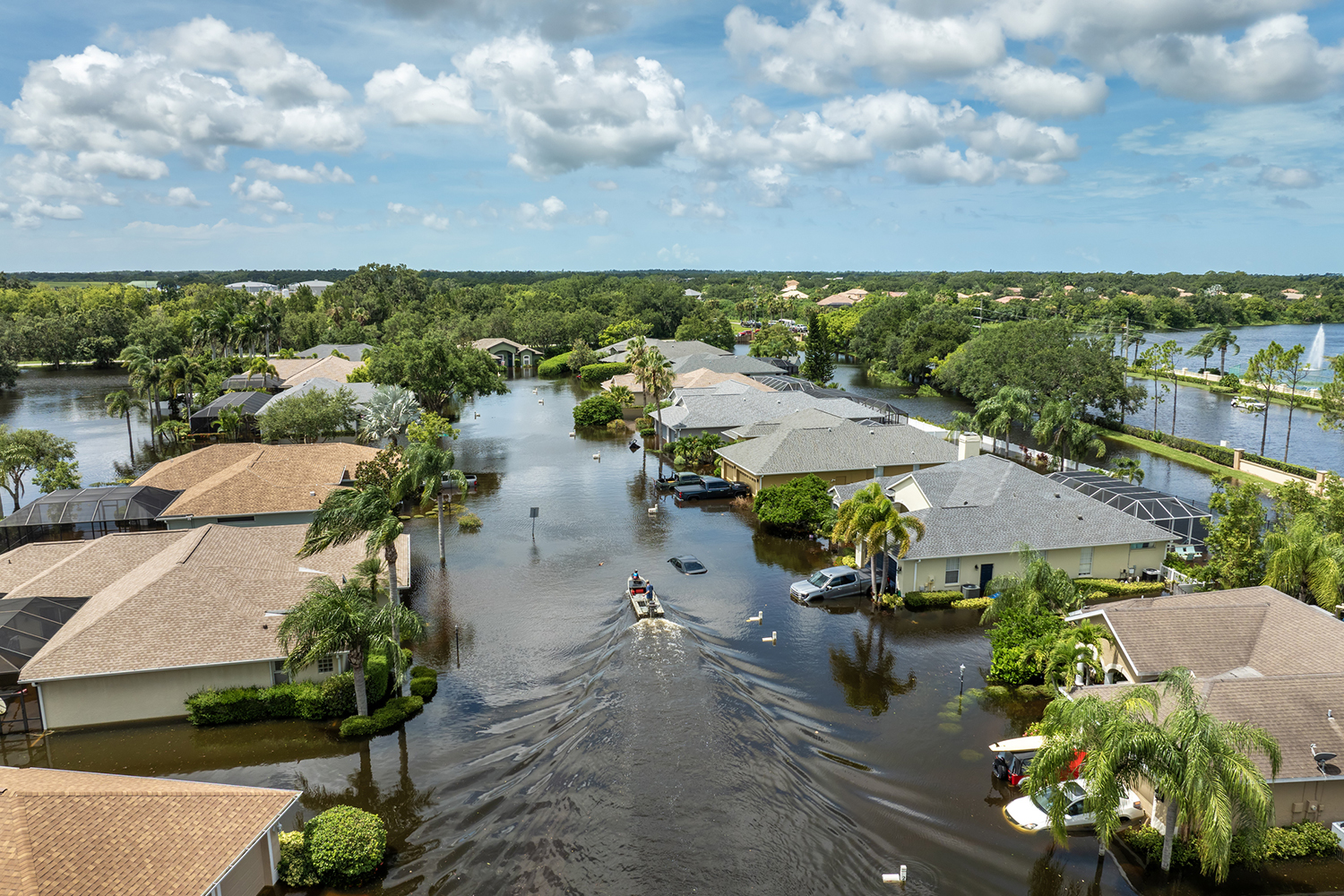 Image of people boating on rainfall flood waters between rural homes in a residential area of Sarasota, Florida, after Hurricane Debby.