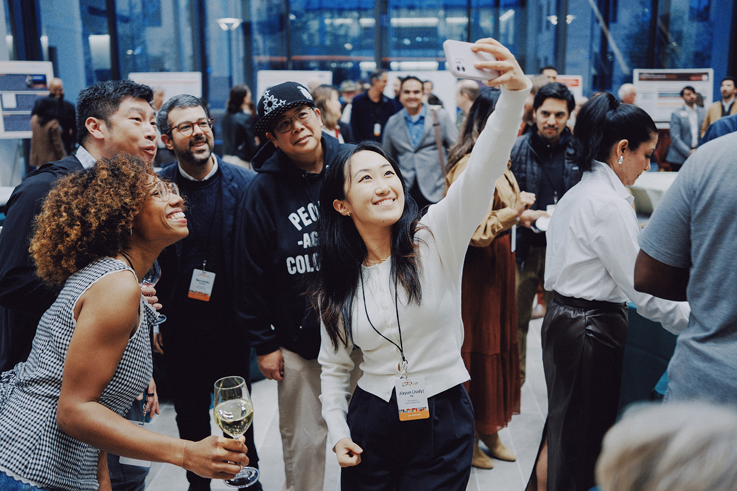 A group of people socialize at an event while one person takes a selfie.