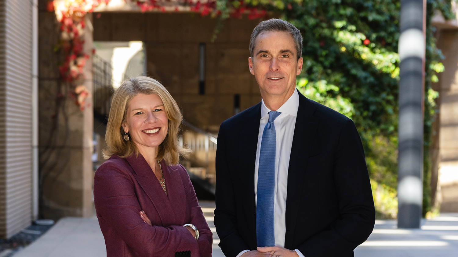 Nora and David Freeman Engstrom stand smiling side by side outdoors on the Stanford campus.