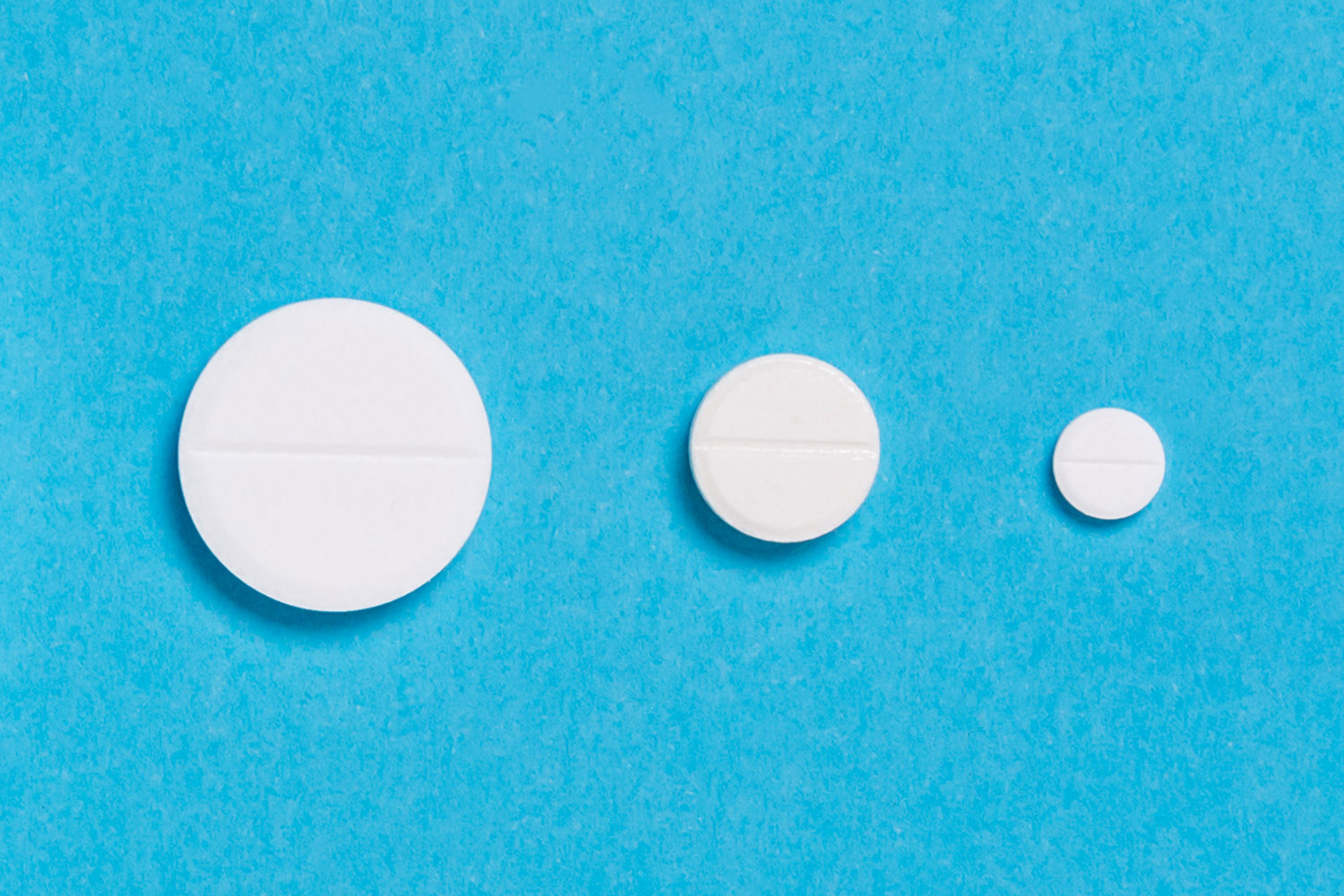 Three white pills of different sizes are lined up on a blue background, showing their decreasing diameters.