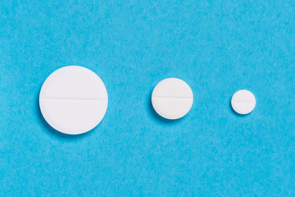 Three white pills of different sizes are lined up on a blue background, showing their decreasing diameters.