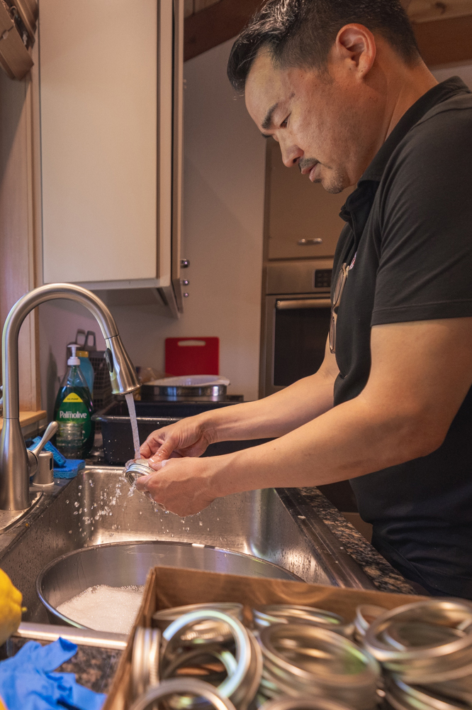 Man washing canning rings and lids at kitchen sink while preparing to make jam.