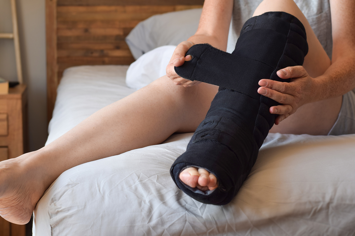 Woman sitting on bed putting on night compression wrap boot on lymphedema affected leg.