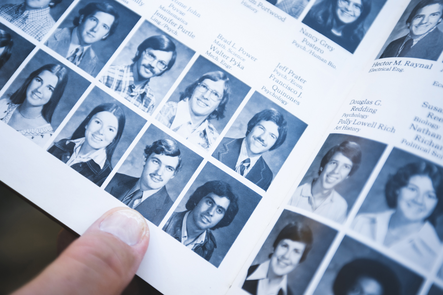 Hand holds open a yearbook page filled with black-and-white senior portraits.