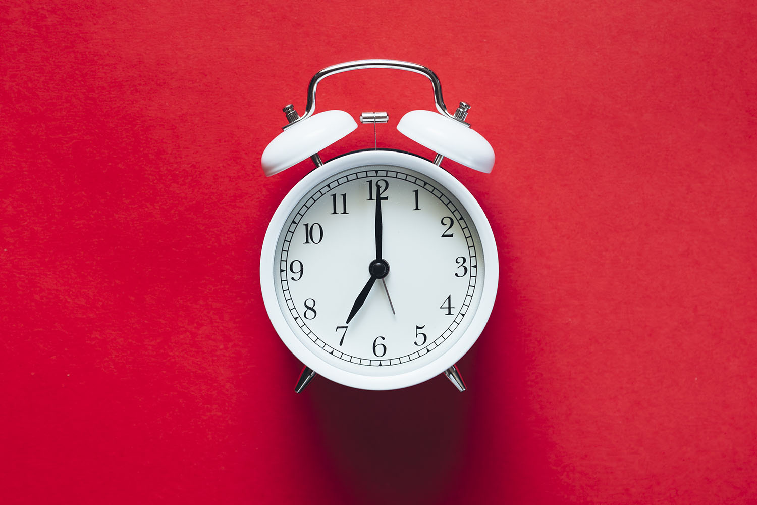 White old-fashioned alarm clock set a 7 o'clock on a red background.