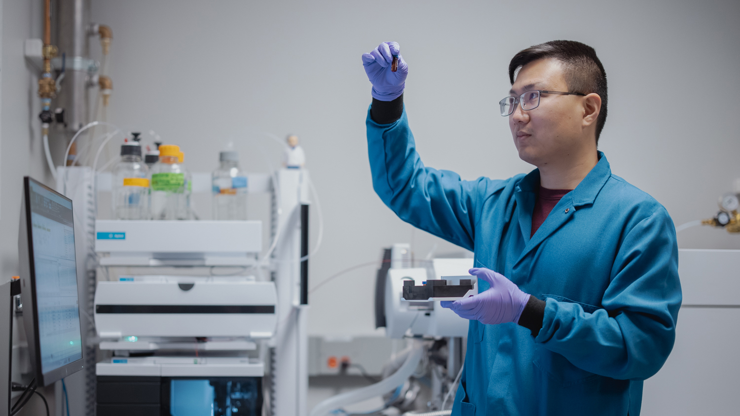 Image of a lab tech examining substance in a vial.