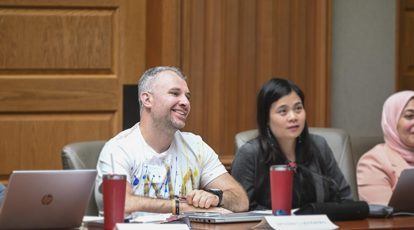 Participants engage in discussion around a meeting table, with a Iaroslav Liubchenko in a paint-splattered shirt and women listening attentively.