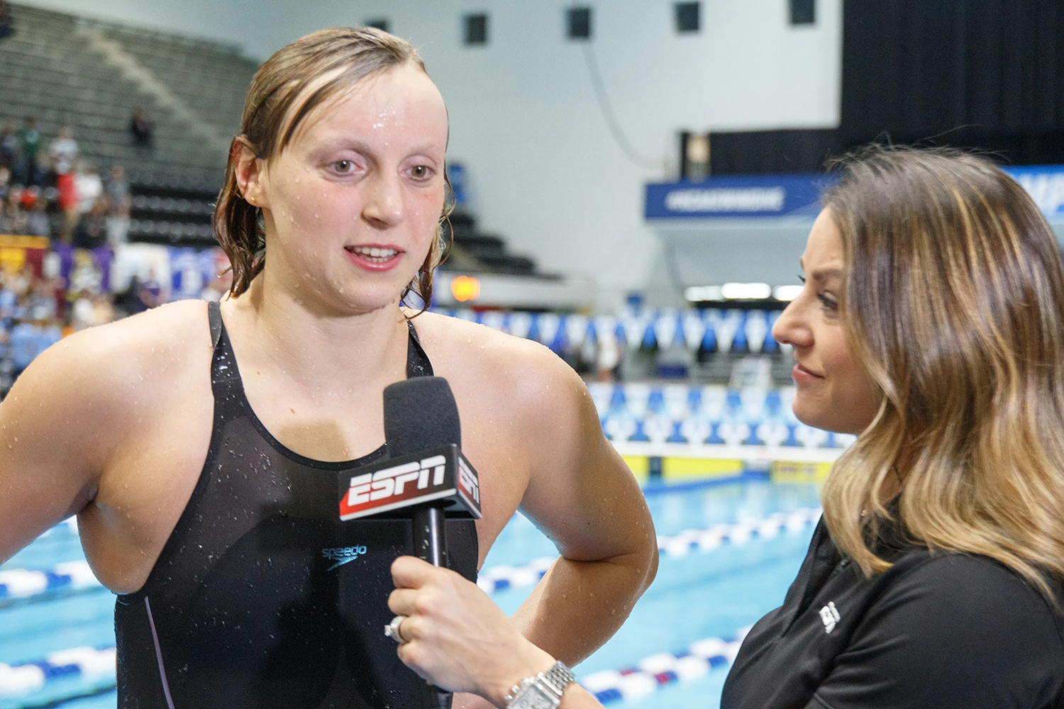Katie Ledecky interviewed by a reporter, with a competitive swimming venue visible in the background.