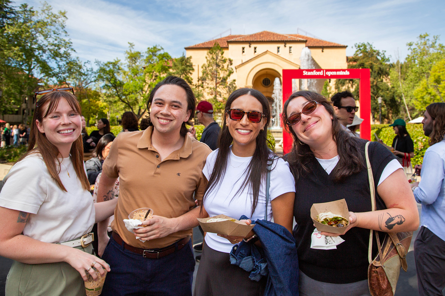 Four people pose together with food during the block party, with a fountain and a red 