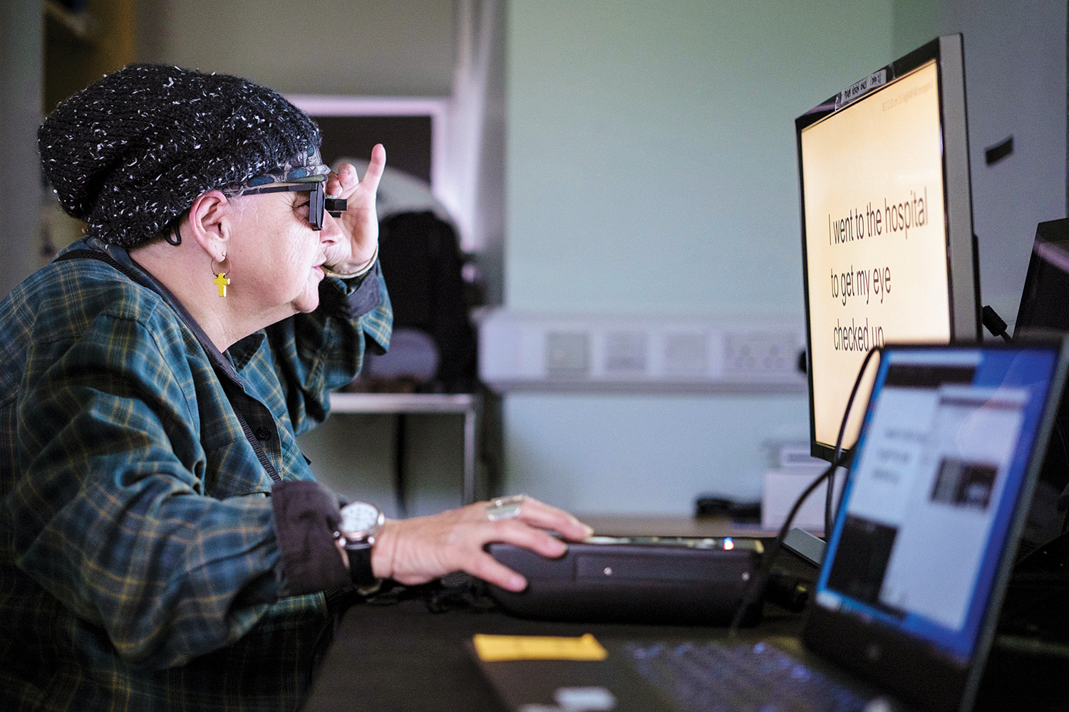 Woman wearing dark glasses uses a large-text computer monitor with assistive technology.