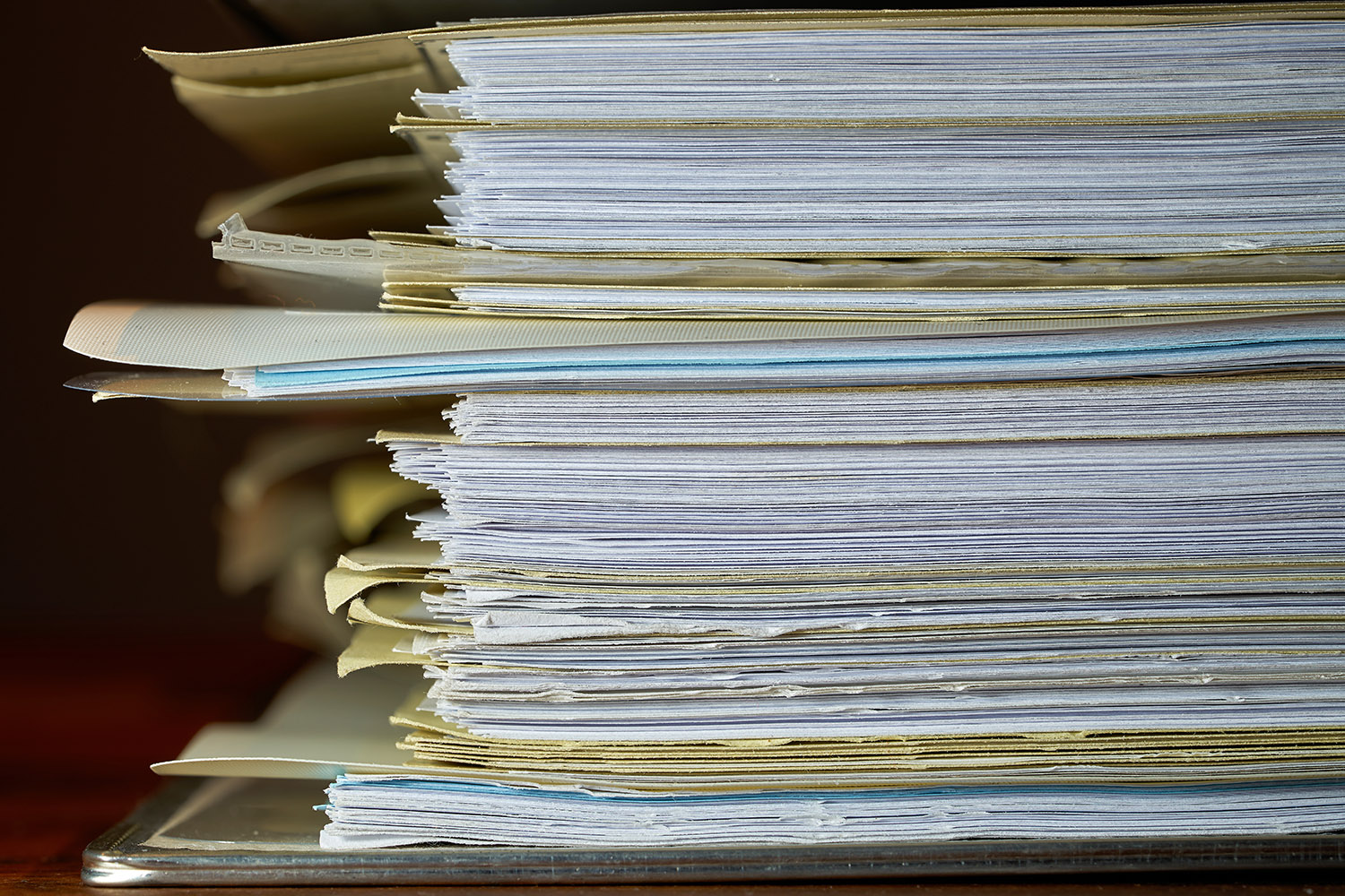 Stack of file folders stuffed with pages piled on a desk.