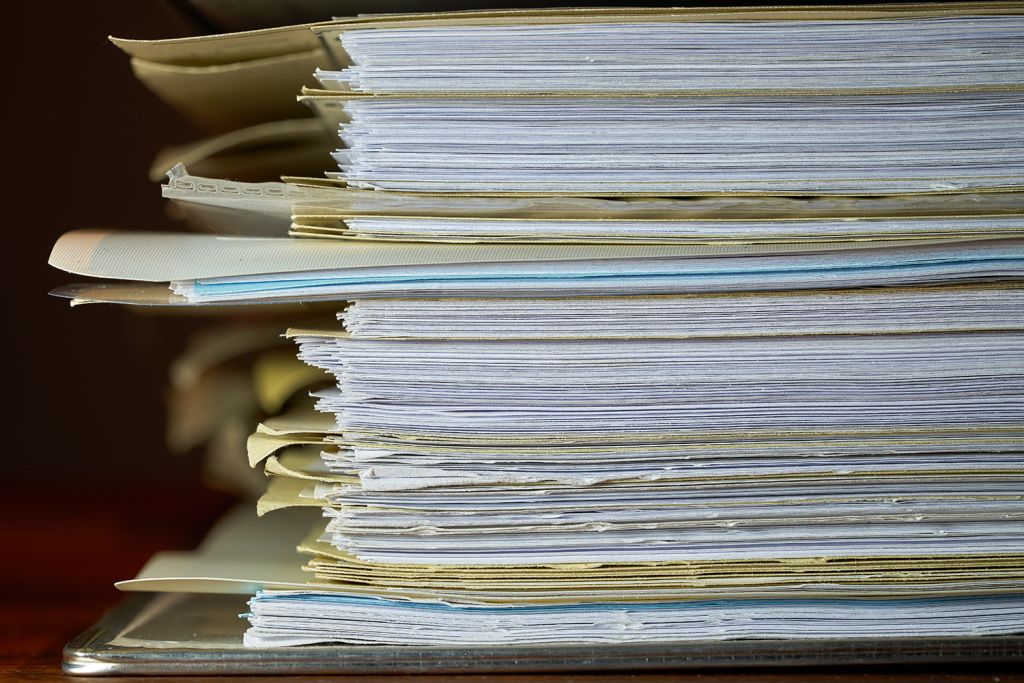 Stack of file folders stuffed with pages piled on a desk.