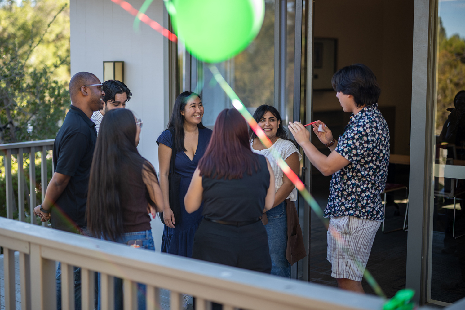 A group of students chat and laughs together on a balcony decorated with balloons.