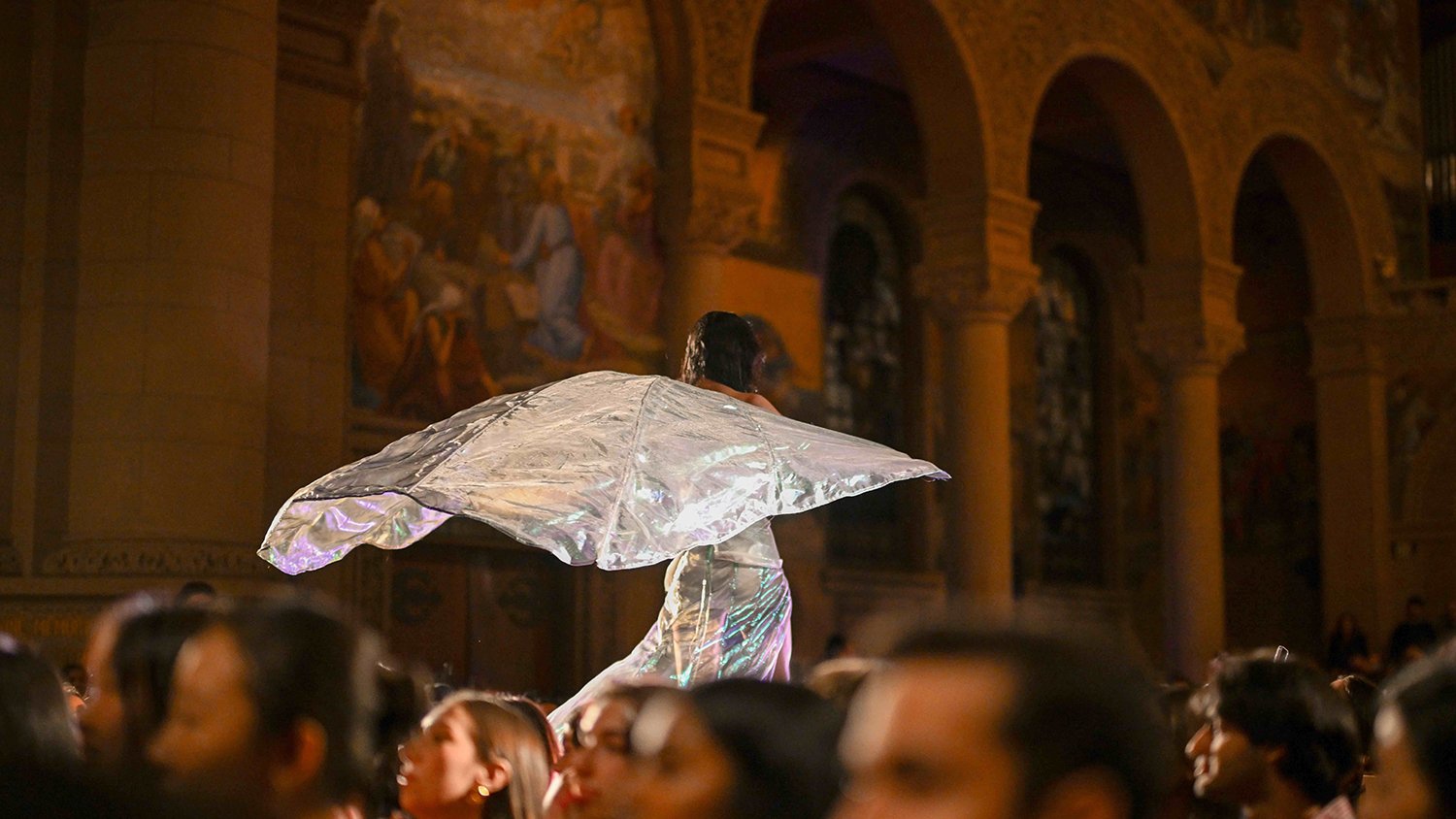 Student model walking down a runway with a silver cape flowing behind them.