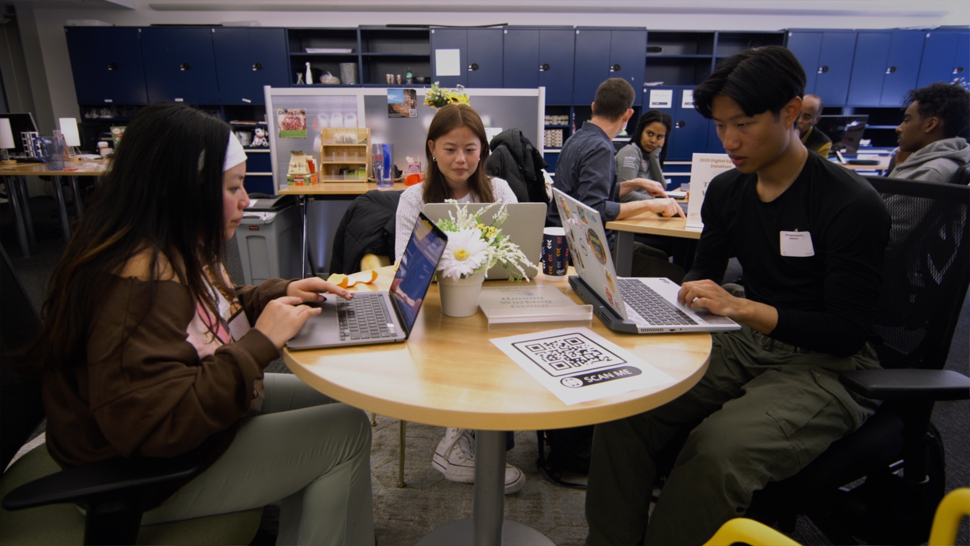 Students gather at a table looking at their laptops.