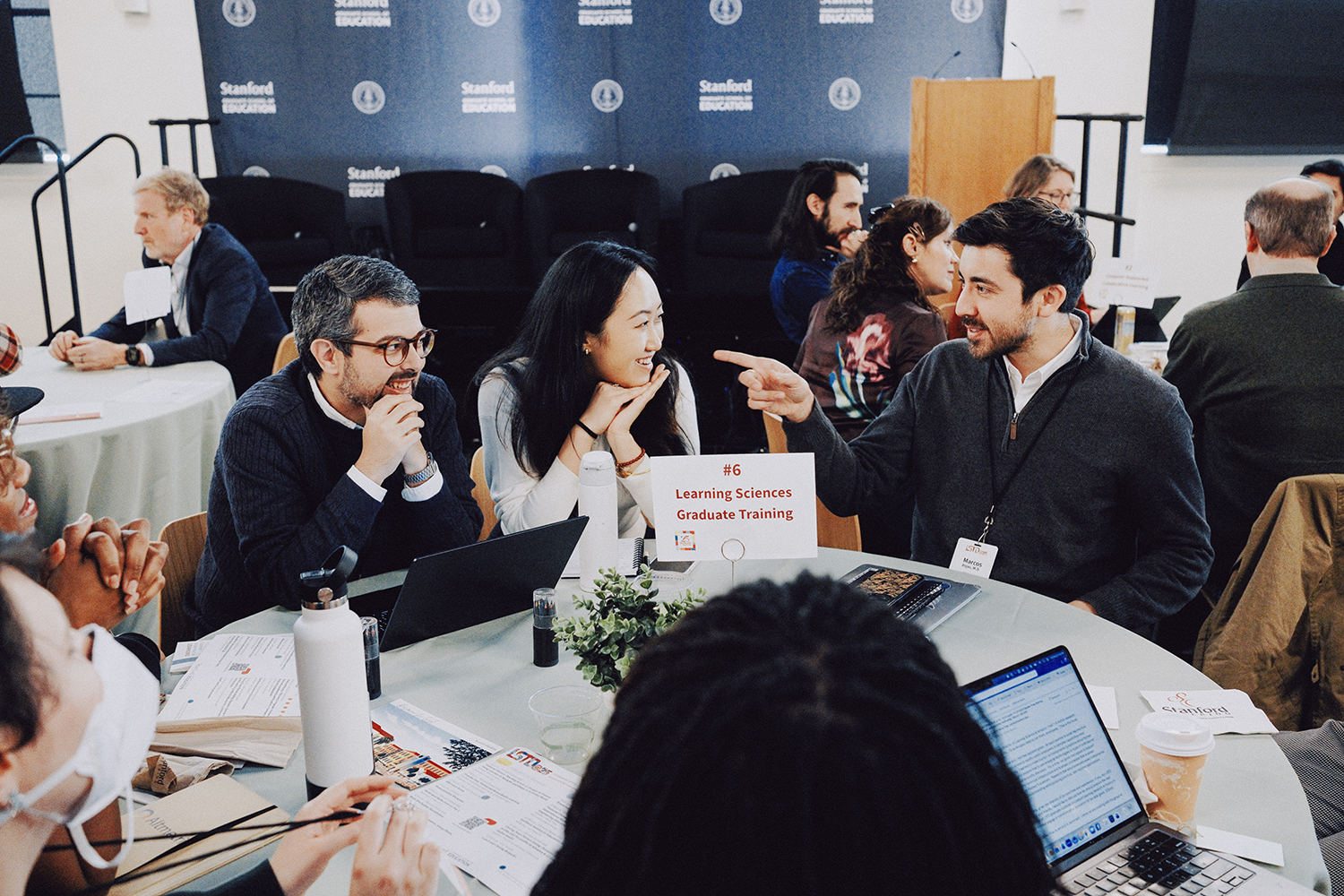 Participants engage in discussion at a roundtable during a Learning Sciences training event, with materials displayed on the table.