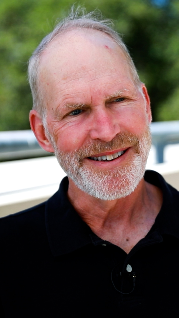 A smiling Rob Jackson with a beard wears a black shirt, appearing relaxed during an outdoor interview setting.