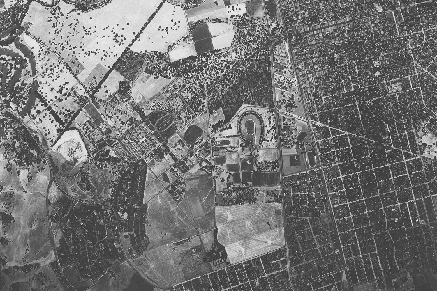 Aerial view of Stanford campus from 1939 showing a mix of agricultural land and urban areas, including a stadium and surrounding neighborhoods.
