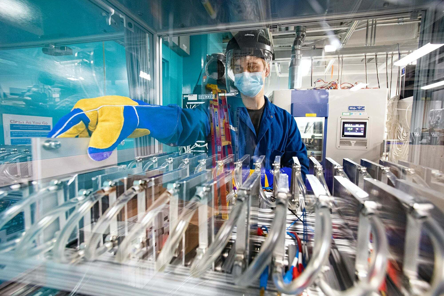A worker in protective gear operates machinery in a cleanroom environment, focused on managing equipment with safety protocols.